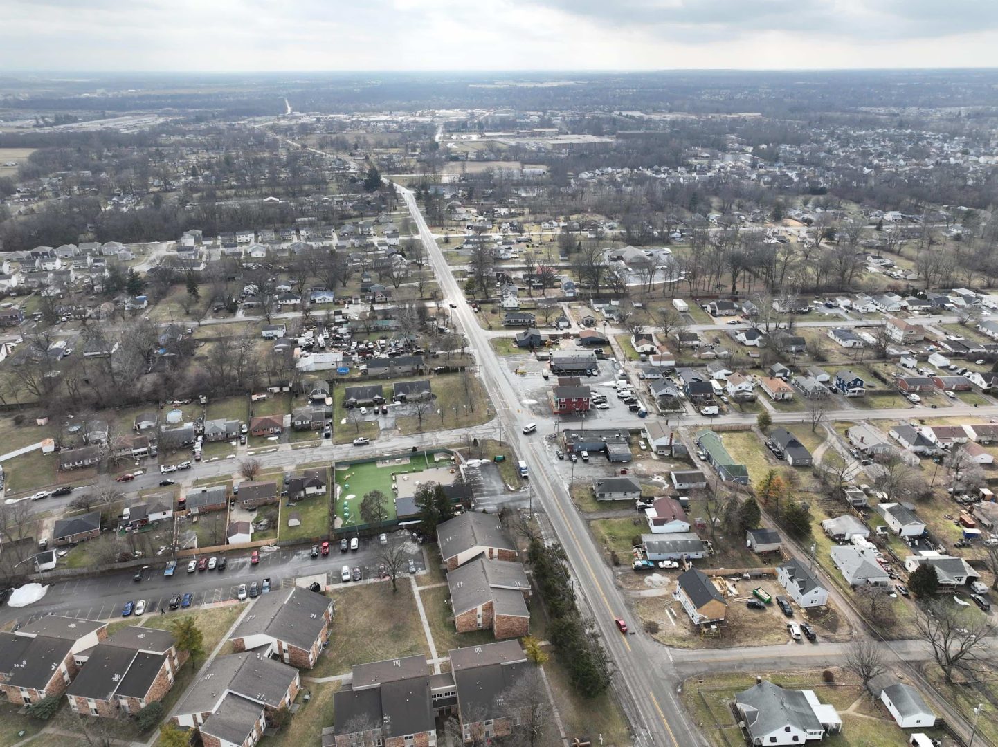Aerial view of a suburban neighborhood with houses, apartments, streets, and sparse trees on a cloudy day. Roads intersect in the center, and the landscape extends into the distance. Aerial view of a suburban neighborhood with houses, apartments, streets, and sparse trees on a cloudy day. Roads intersect in the center, and the landscape extends into the distance.