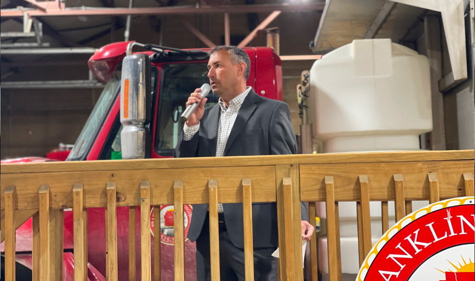 Picture of Adam Fowler speaking with a microphone in front of a truck